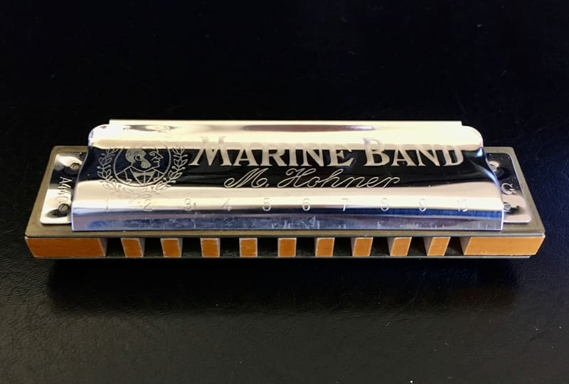 Ten-hole diatonic harmonica with a chrome cover plate engraved with the Marine Band name, and wooden comb and reed plate visible from the front edge, on a black background.
